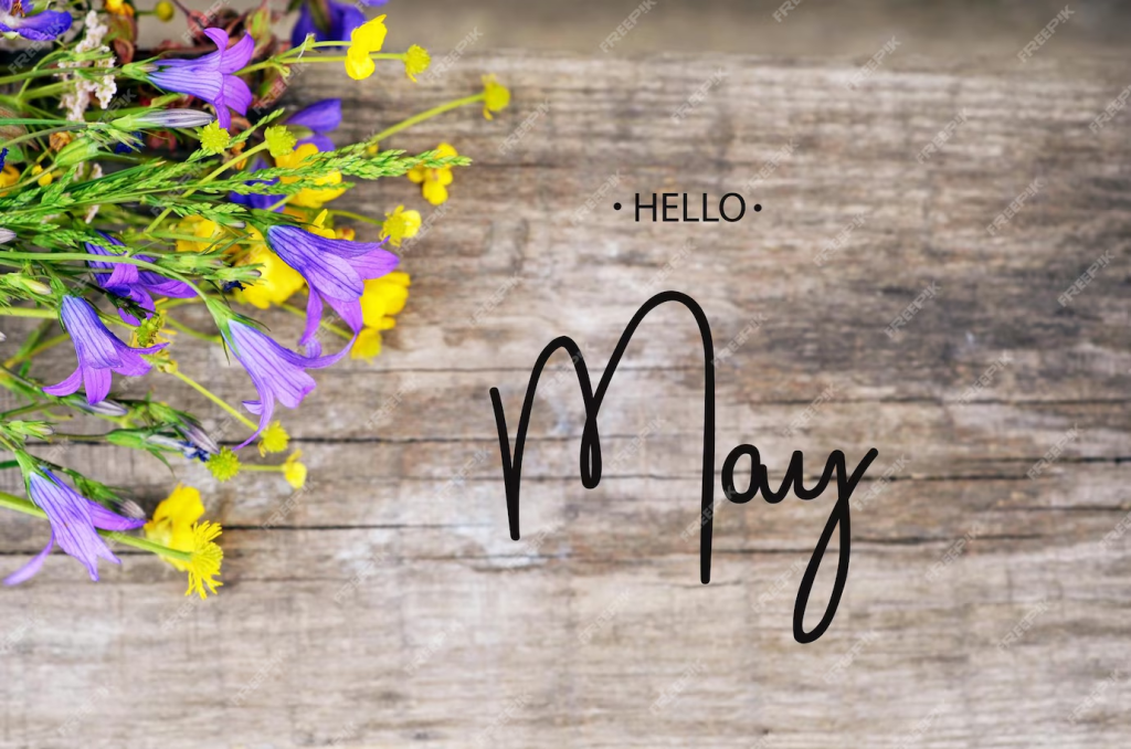A bouquet of colorful wildflowers arranged on a wooden surface with the text 'Hello May' elegantly scripted.