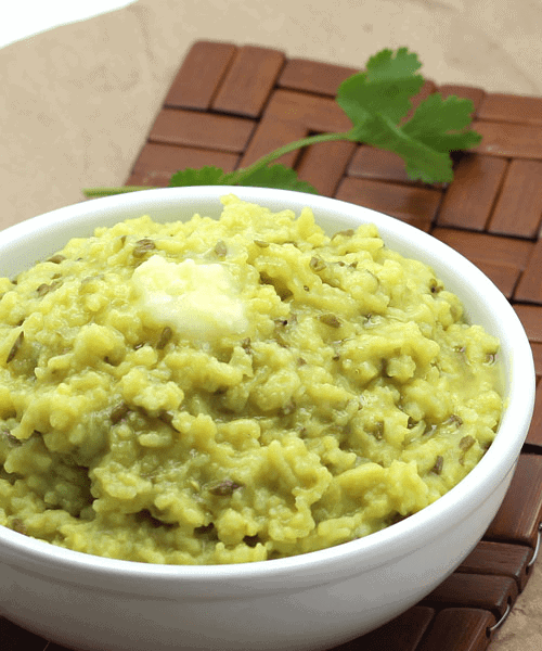 A bowl of khichdi with a dollop of butter on top, served on a wooden mat, garnished with fresh cilantro.