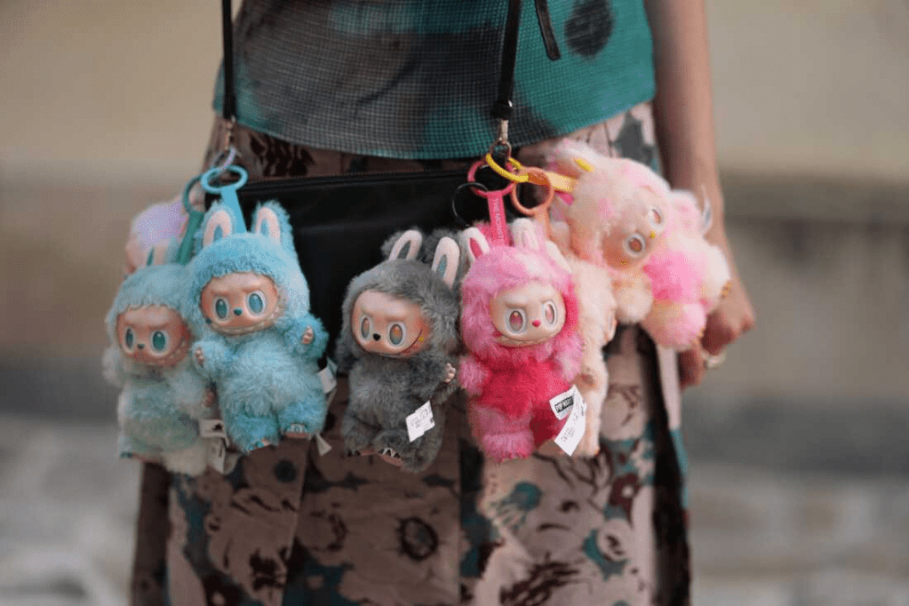 A person holding a bag adorned with multiple Labubu plush keychains in various colors, including blue, gray, and pink, showcasing their playful design.